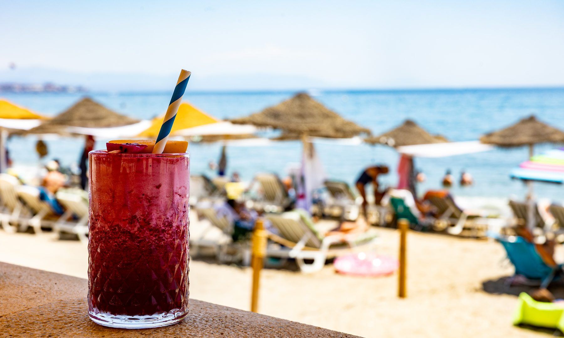 A berry drink on the sea wall, straw parasols and the Mediterranean behind.